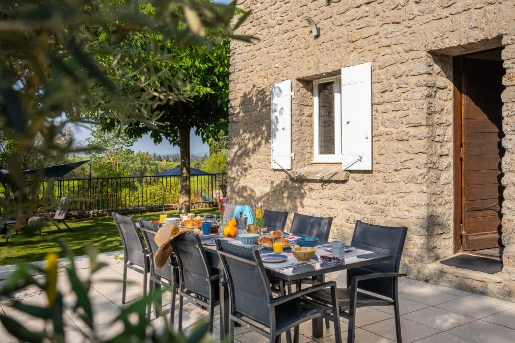 Petit-déjeuner en terrasse, table dressée, maison en pierre.