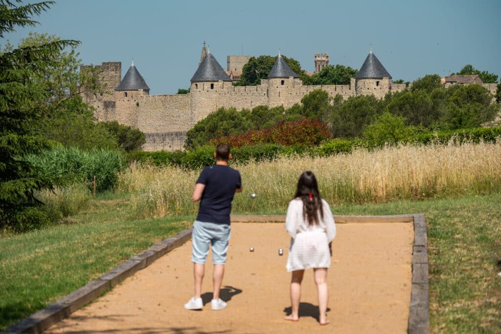 Deux personnes jouent à la pétanque devant un château.