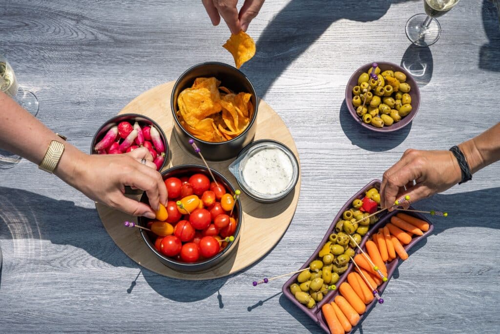 Apéro avec légumes, chips et olives sur table extérieure.