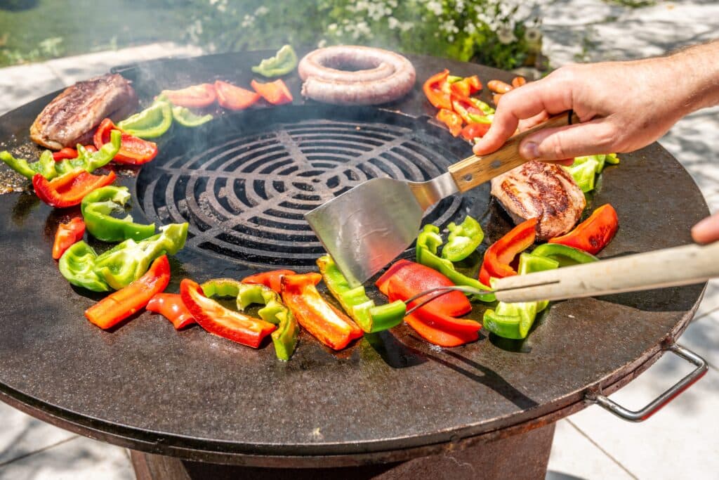 Cuisson de légumes et viande sur barbecue rond.