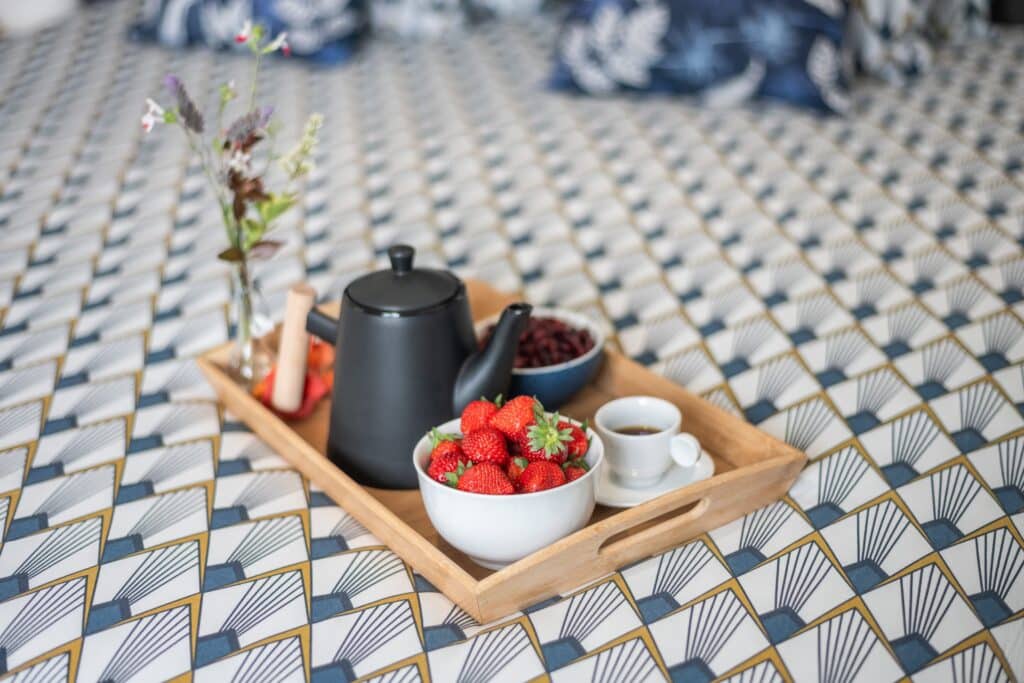 Plateau avec théière, fraises et fleurs sur une table.