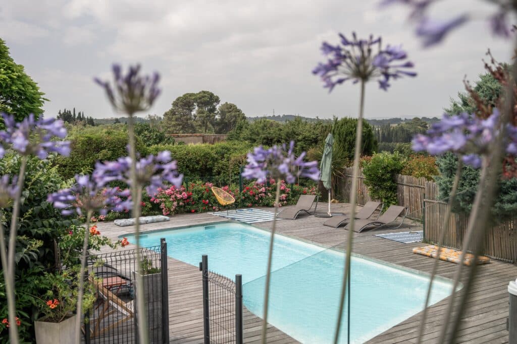 Piscine extérieure avec transats et fleurs violettes.
