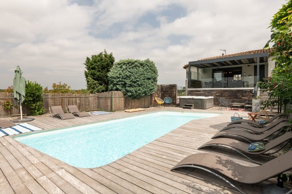 Piscine extérieure avec terrasse en bois et chaises longues.