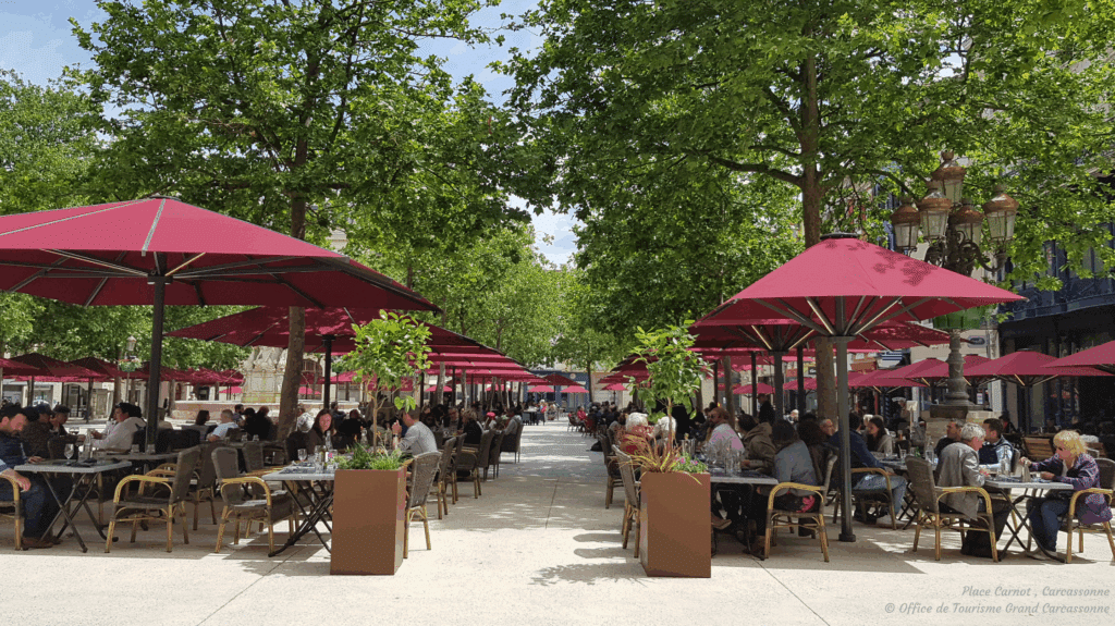 Terrasse animée sous parasols rouges, Place Carnot Carcassonne.