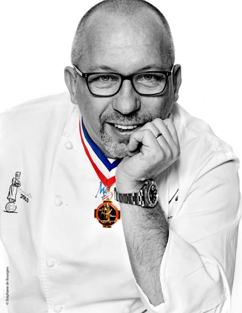 Chef souriant avec une médaille et lunettes.