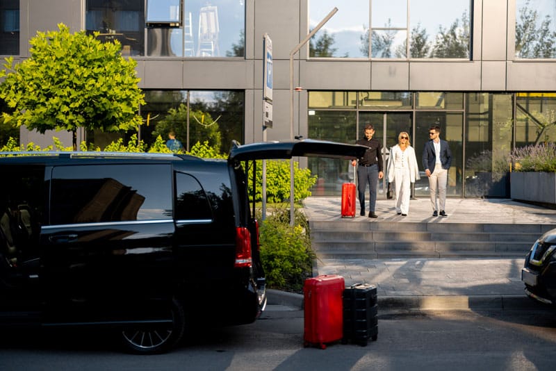 Personnes avec valises rouges près d'un van noir.