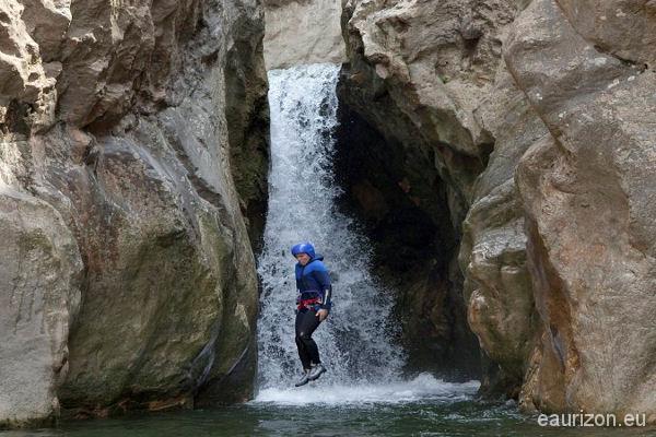 Canyoning : homme traversant cascade en combinaison.