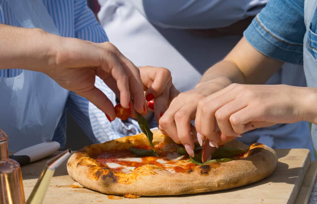 Mains préparant une pizza avec tomate et basilic