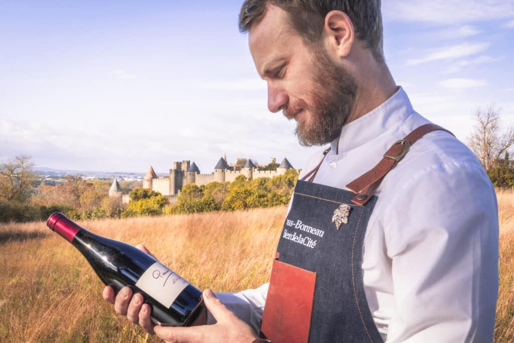 Homme admirant une bouteille de vin devant un château.