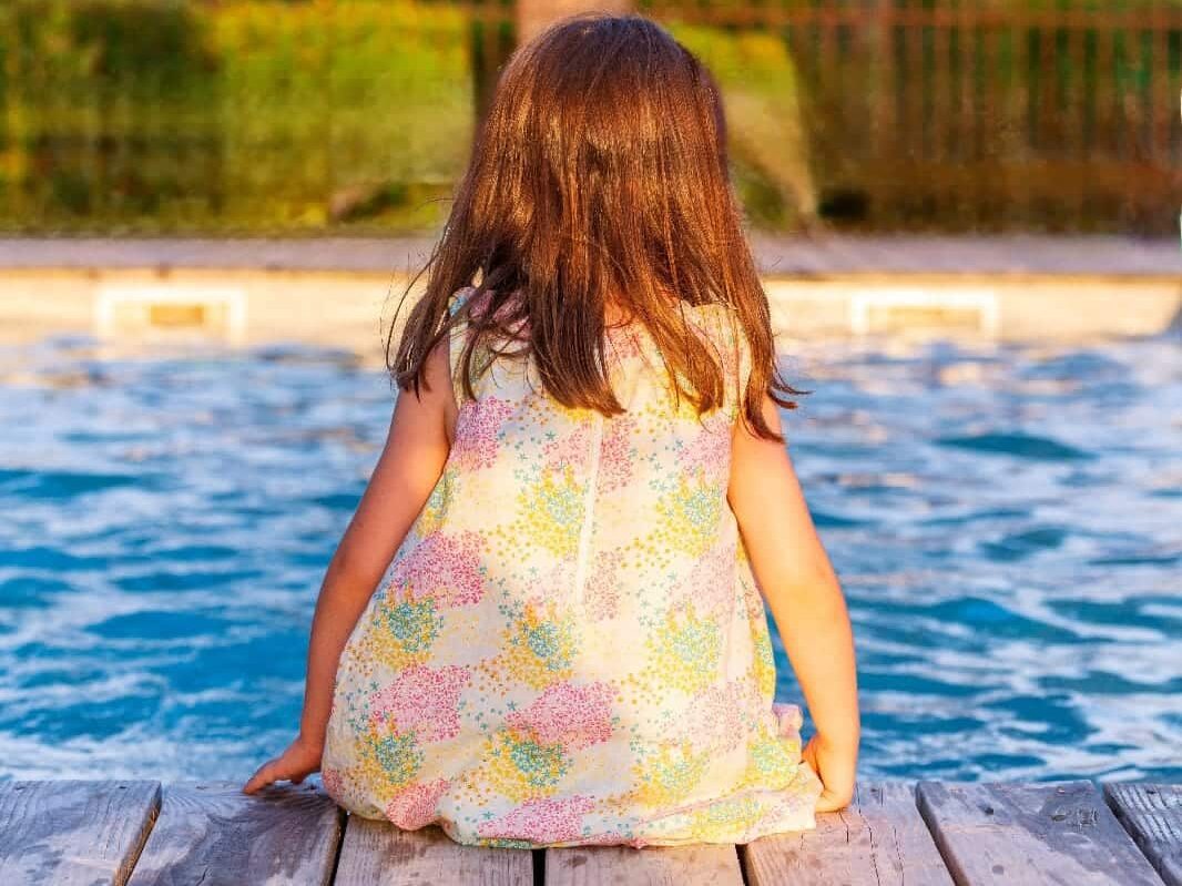 Enfant assise au bord d'une piscine en bois.