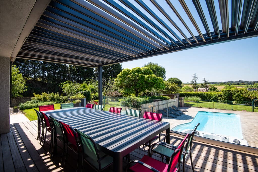 Terrasse ombragée avec piscine et jardin verdoyant.